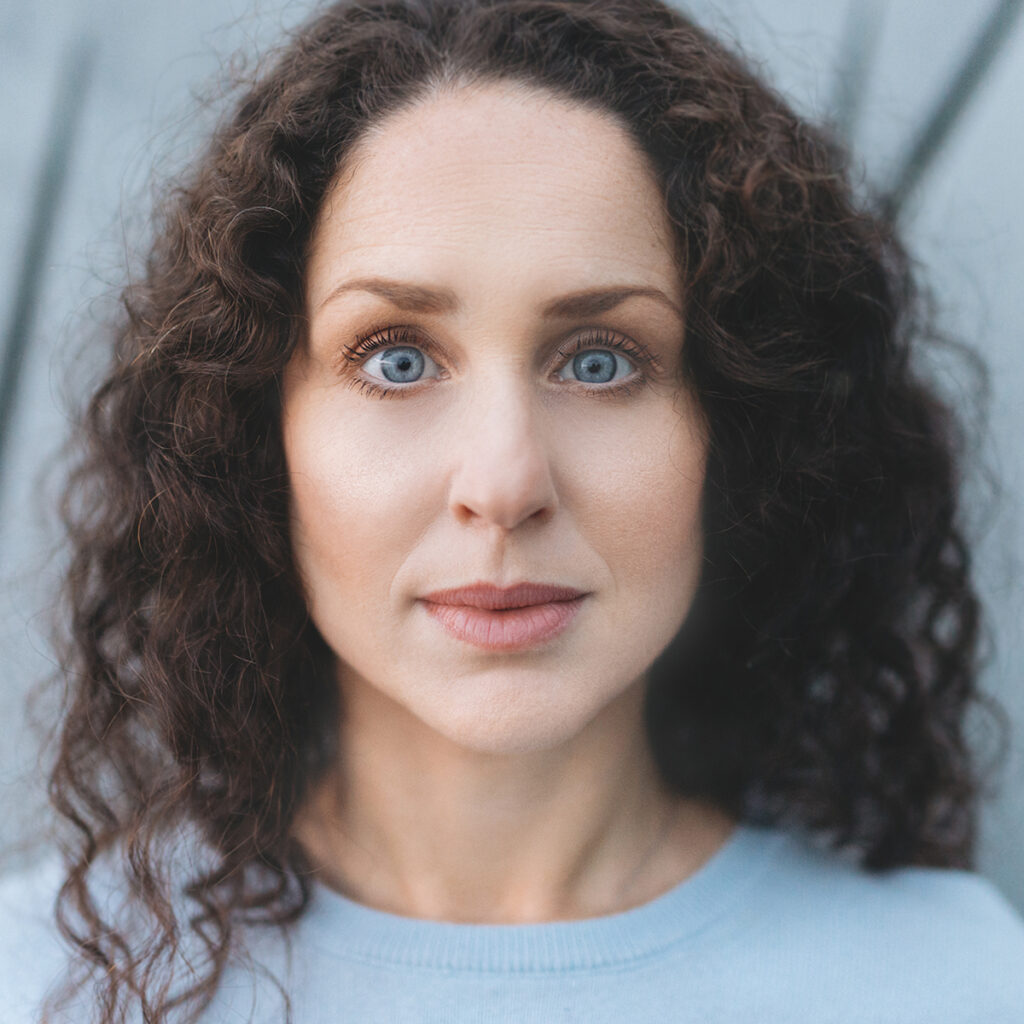 Sara Sommerfeld sitter leende i lotusställning vid vattnet under en porträttfotografering av porträttfotograf Sussie Mellstedt, Sussie Mellstedt Photography, Stockholm.